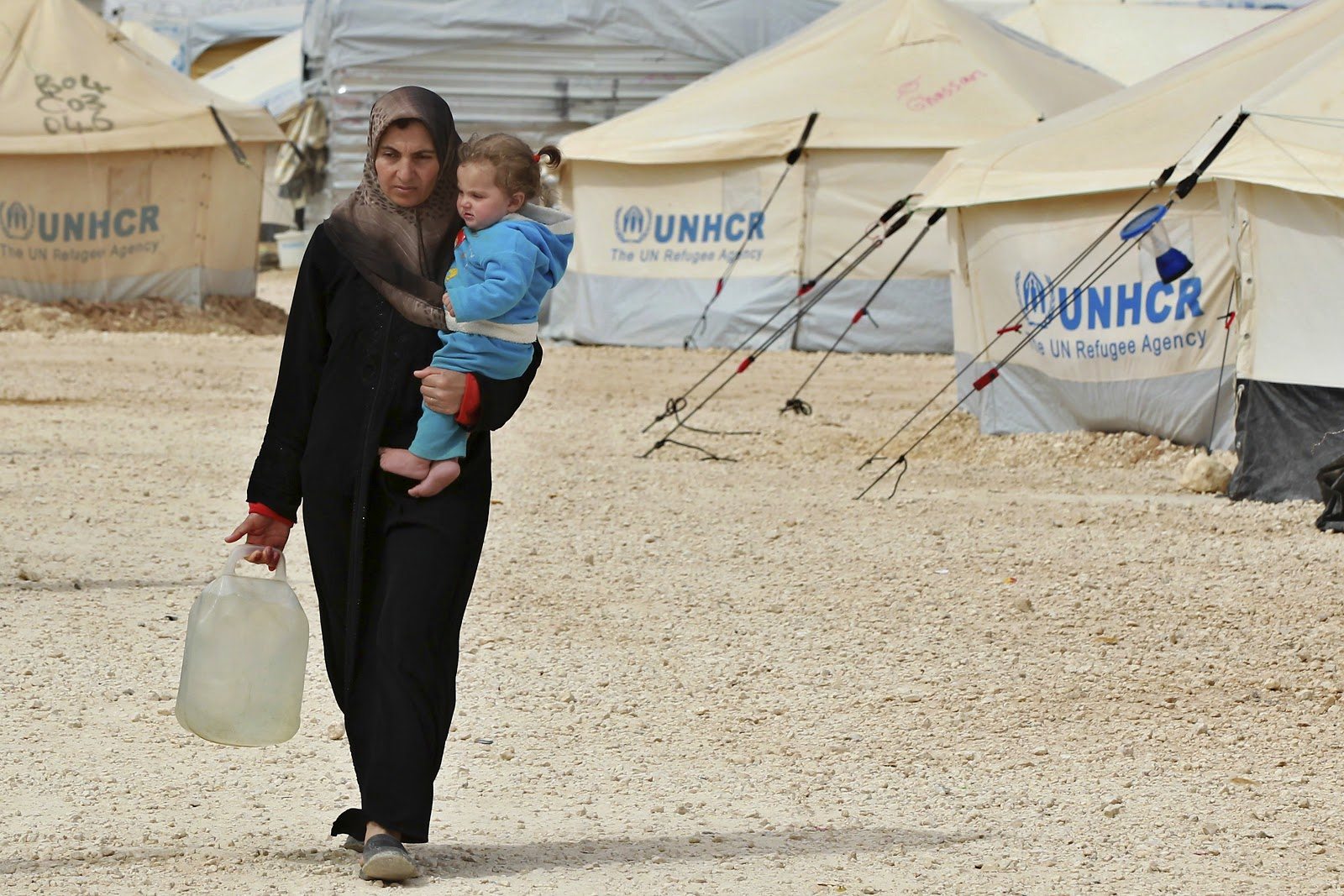 Image A Syrian refugee woman carries her daughter as she walks with a container after collecting water at the Al Zaatri refugee camp in the Jordanian city of Mafraq, near the border with Syria. (REUTERS / Muhammad Hamed)