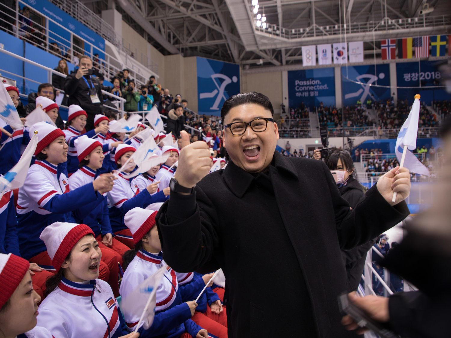 Image A man impersonating Kim Jong Un in front of the North Korean cheerleaders at an Olympic women's ice hockey game at the South Korean Olympics. The blurred hands on the side of the image are North Korean “minders” moving in to whisk him away. (Yelim Lee/AFP)