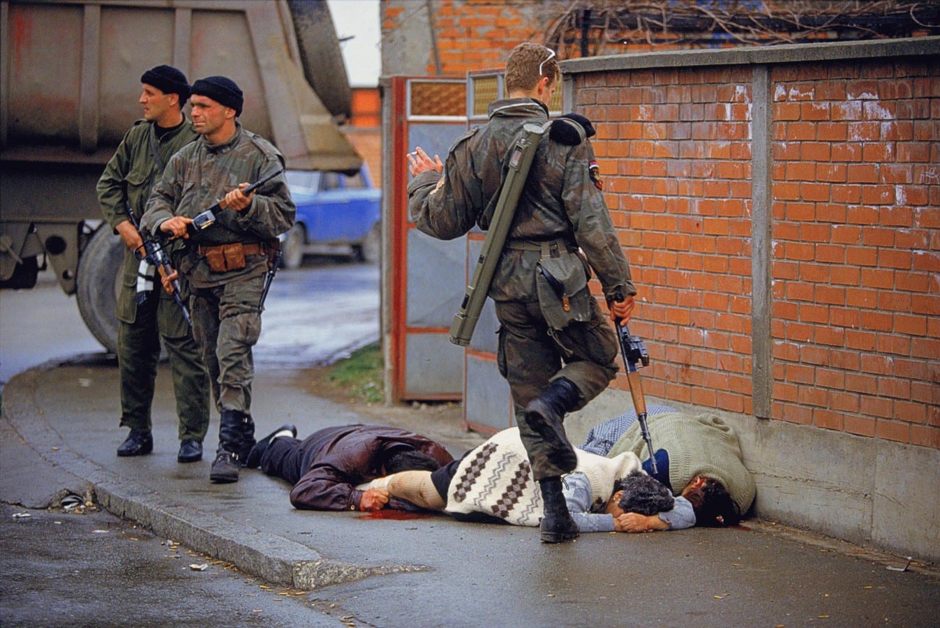 Image [A member of the Serb nationalist militia known as the Tigers, led by Zeljko Raznatovic ("Arkan"), under the command of the Yugoslav People's Army (JNA) controlled by Serbian President Slobodan Milošević, kicks a Muslim woman (Ajsa Sabanovic, white sweater) who had been shot and killed by Serb forces during the Bijeljina massacre, April 1-2, 1992 (Photo: Ron Haviv)]