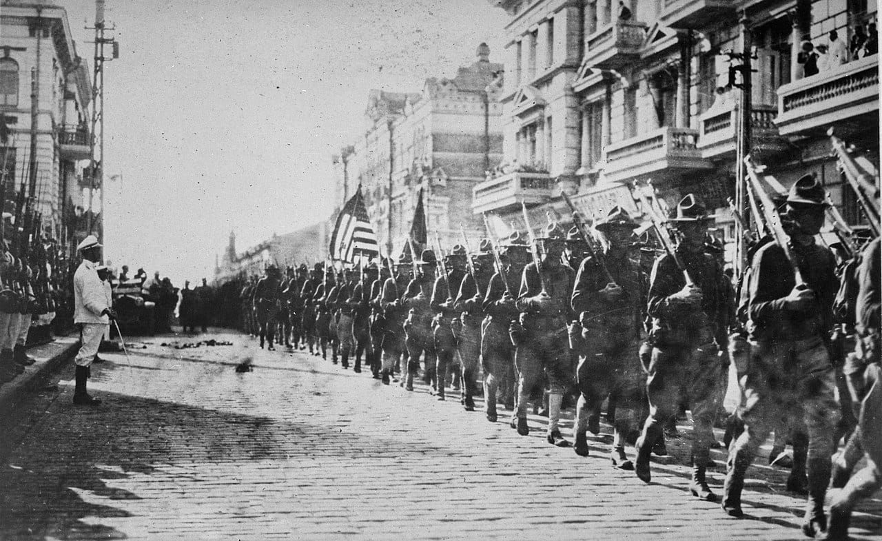 Image American troops in Vladivostok parading before the building occupied by the staff of the Czecho-Slovaks. Japanese marines are standing to attention as they march by. Siberia, August 1918. NARA.